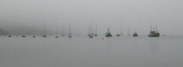 small boats and sailing yachts on flat water in the mist at ullapool harbour